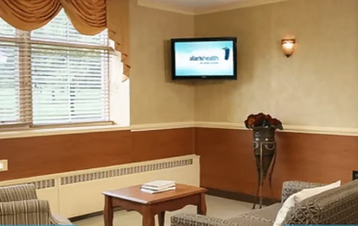 A cozy living room with a wall-mounted television, comfortable seating, and a window with blinds.