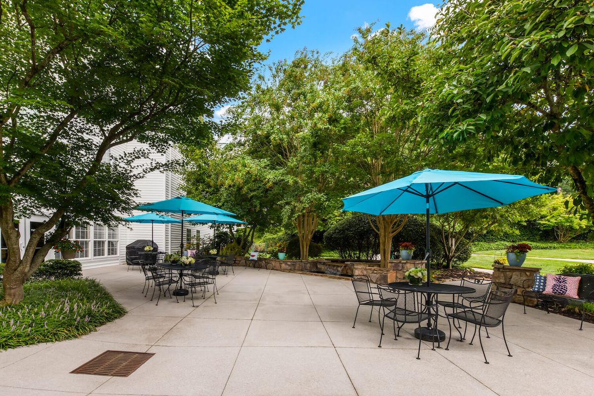 A peaceful outdoor patio with tables, chairs, and bright blue umbrellas surrounded by lush greenery.
