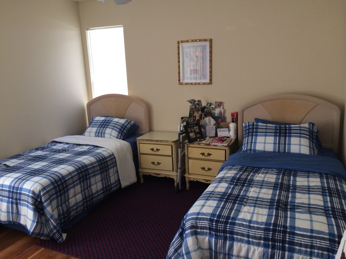 A cozy bedroom with two single beds featuring blue plaid bedding, a nightstand between them, and a window allowing natural light to brighten the room.