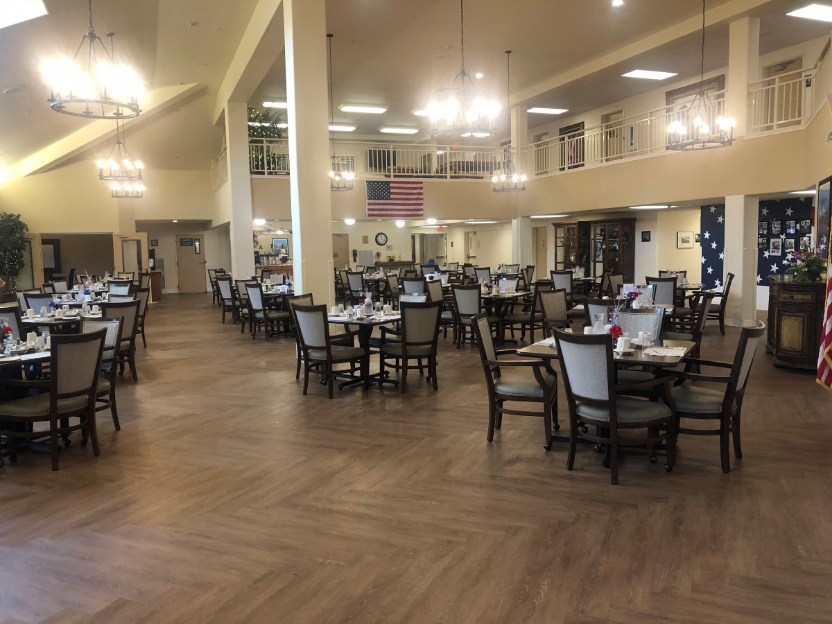 A spacious dining hall with neatly arranged tables and chairs under elegant chandeliers.