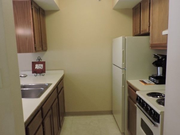 A compact kitchen with wooden cabinets, a refrigerator, and a stove.