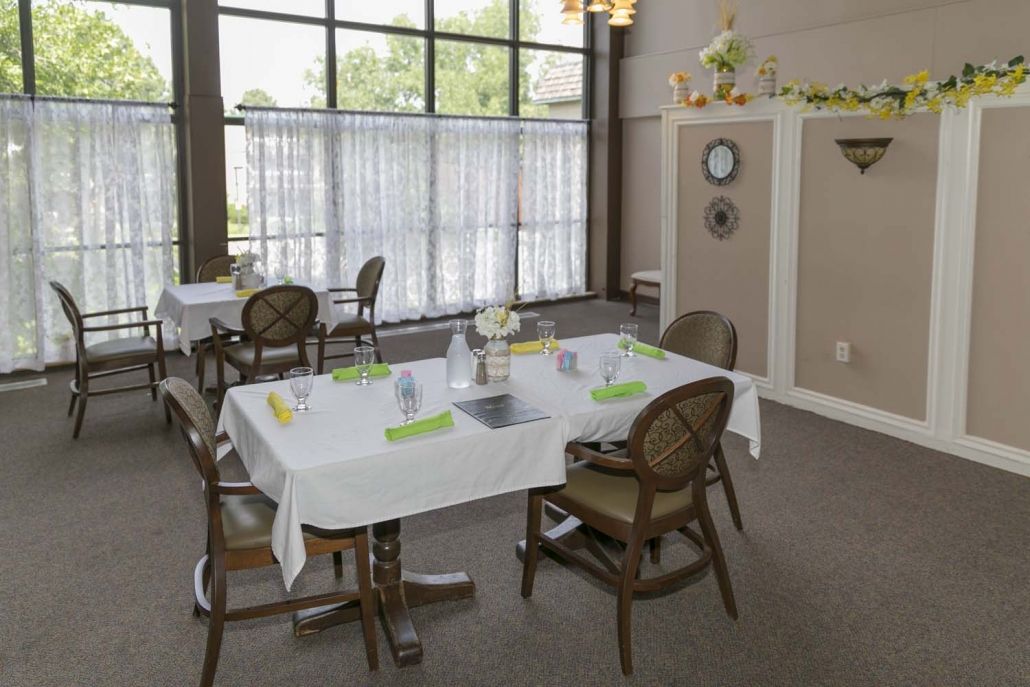 A cozy dining area with elegantly set tables and comfortable seating, overlooking a large window with sheer curtains.