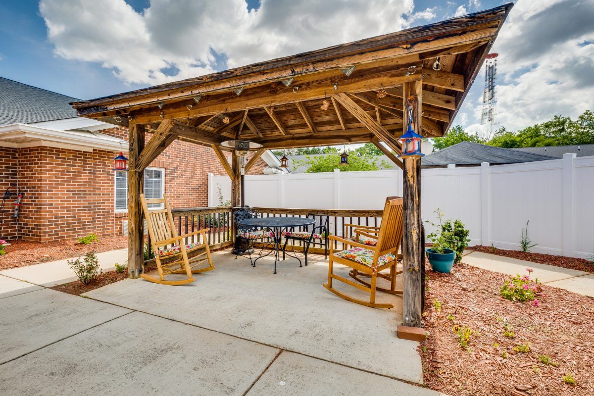 A cozy backyard pergola featuring wooden rocking chairs and a bench under a rustic structure.