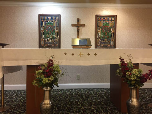A serene altar setup with a cross and decorative art, surrounded by floral arrangements.