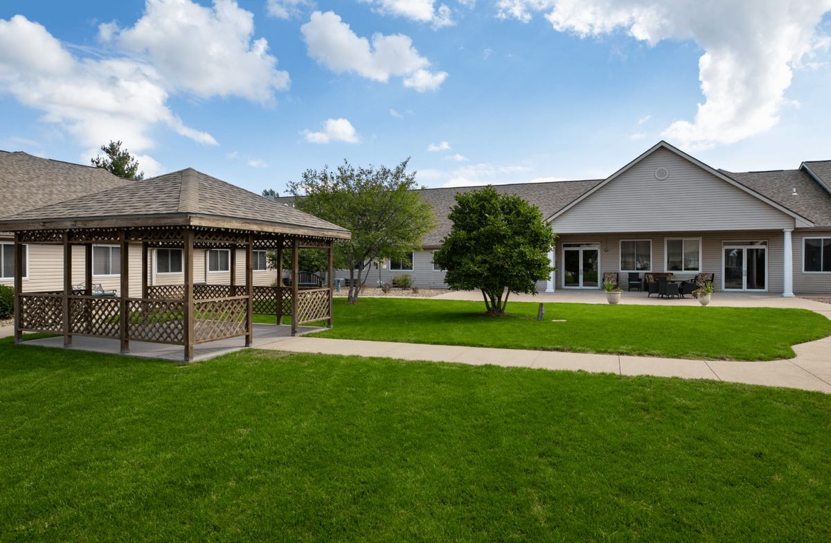 A spacious backyard with a gazebo, lush lawn, and a house under a partly cloudy sky.