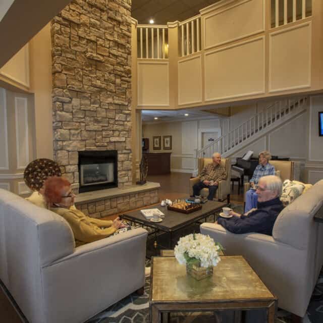 A cozy living room with a stone fireplace and people engaging in conversation.