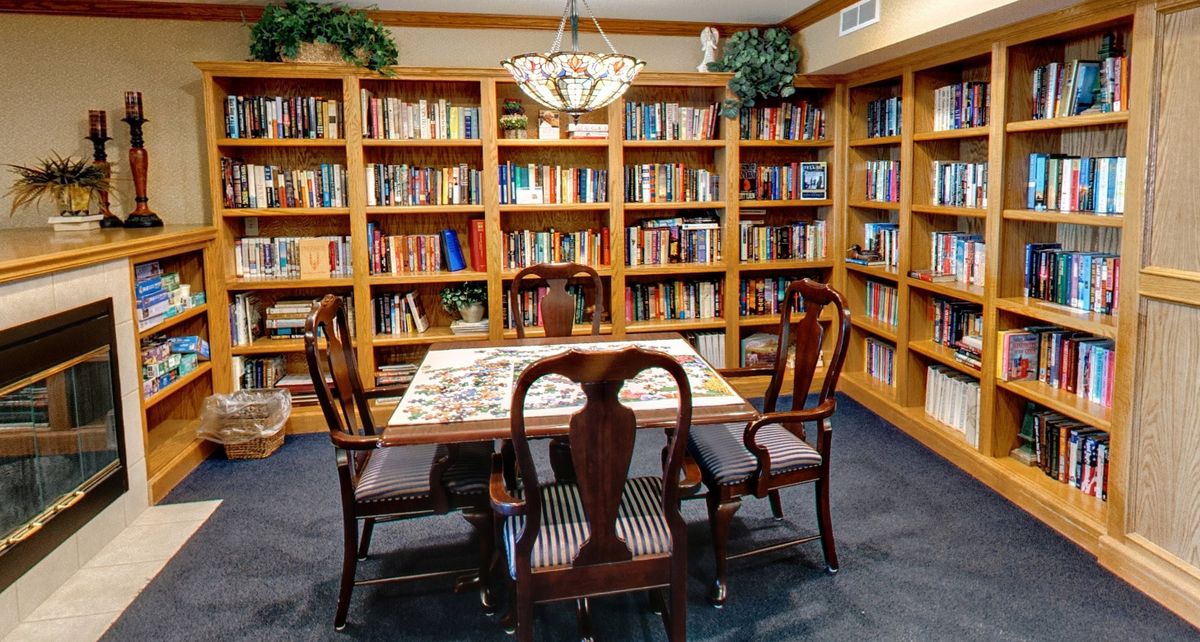A cozy library with wooden bookshelves and a table with chairs in the center, perfect for reading and study.