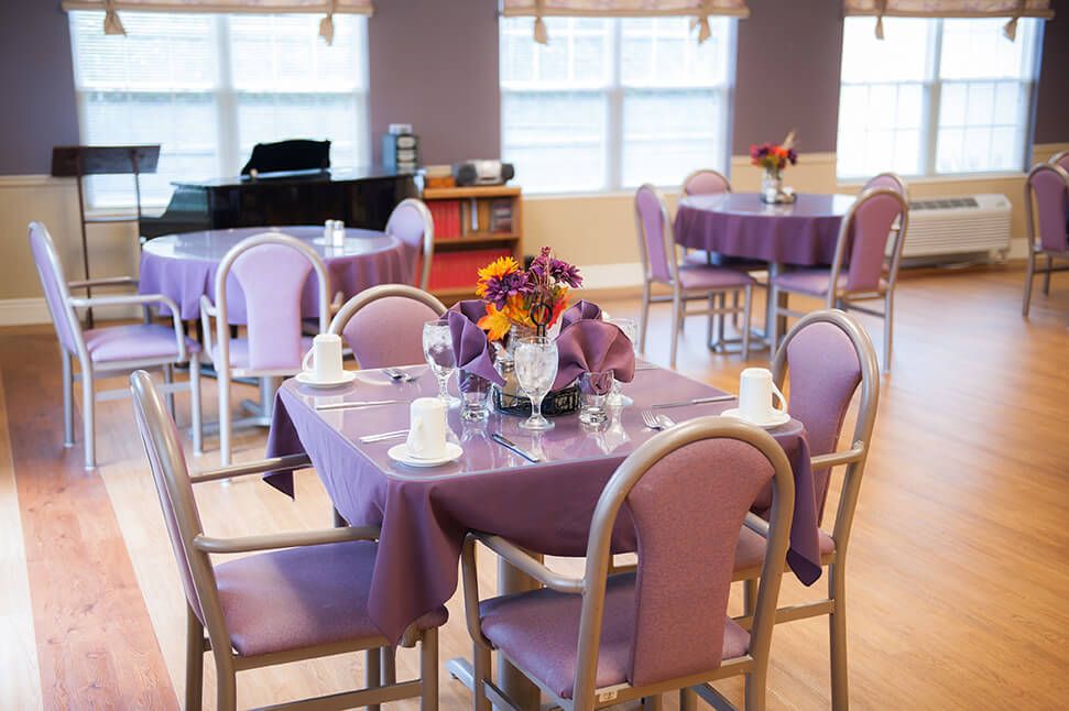 A cozy dining room with purple-themed table settings and a piano in the background.