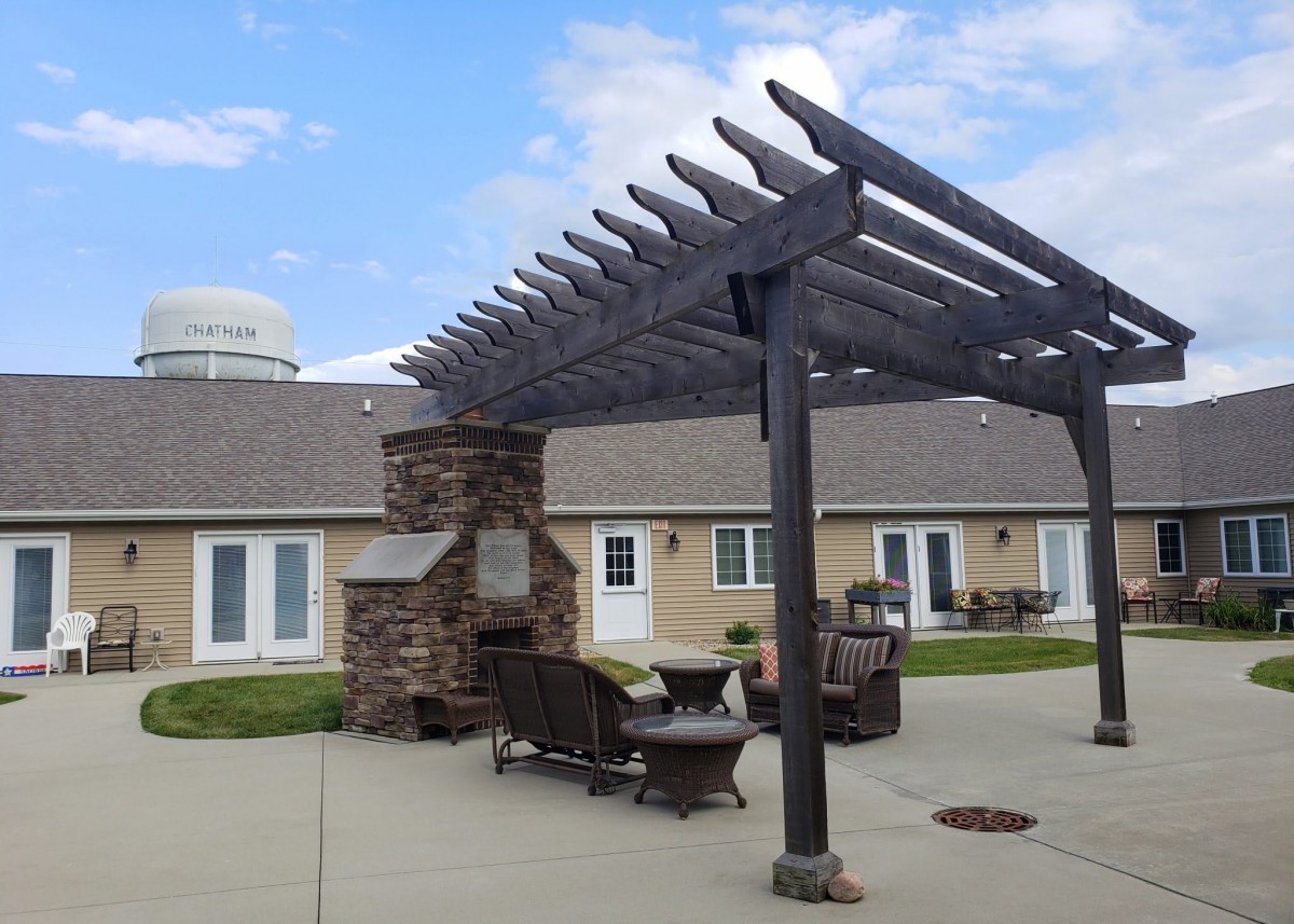 A cozy outdoor patio area featuring a pergola and a stone fireplace, surrounded by comfortable seating.