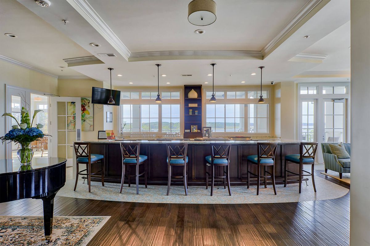 A modern kitchen featuring a bar counter with several stools and pendant lighting, complemented by large windows and hardwood flooring.