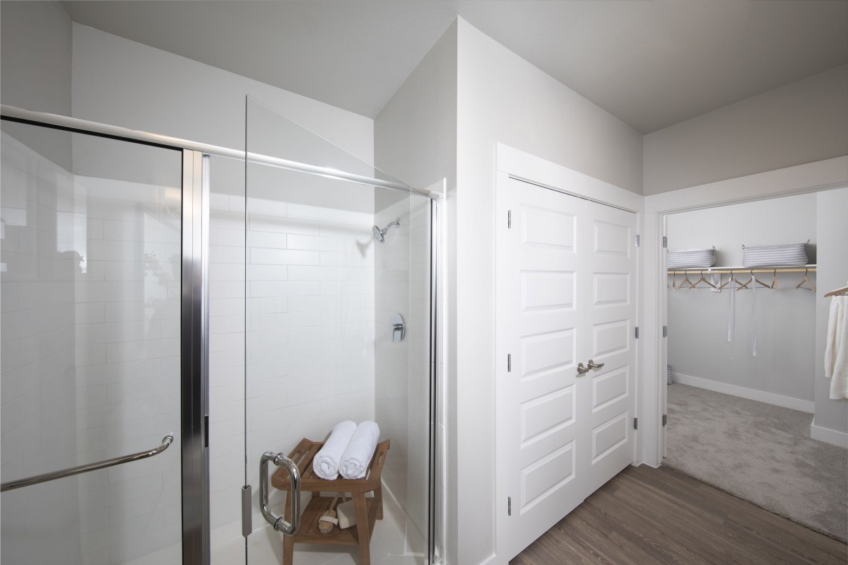 A modern bathroom with a glass shower door, wooden bench, and neatly folded towels.