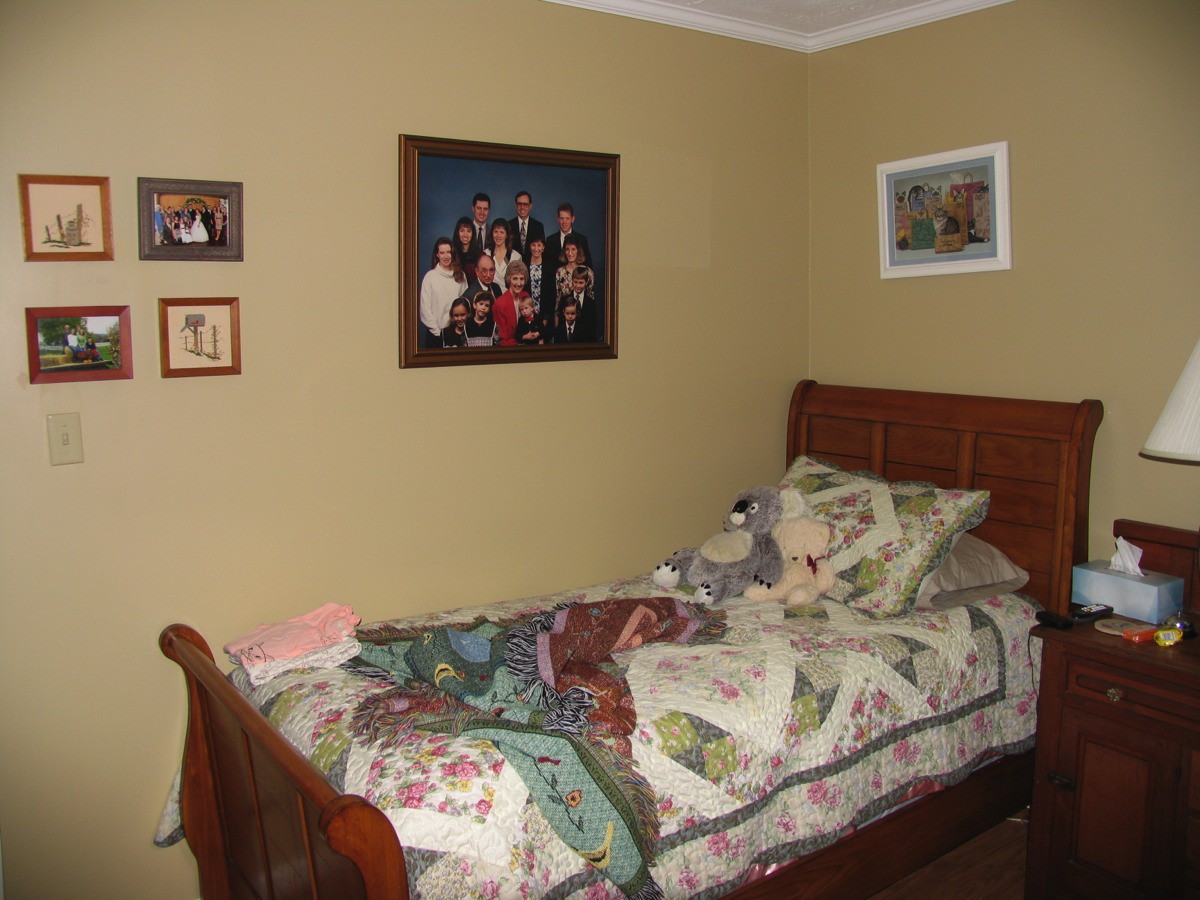 A cozy bedroom with a single bed adorned with a colorful quilt and pillows, complemented by family photos decorating the walls.