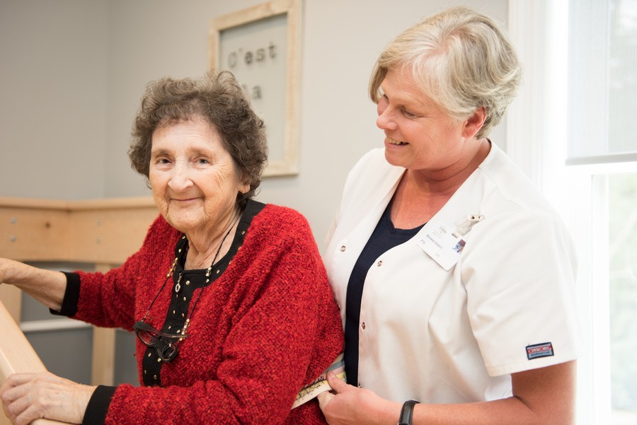 A nurse provides support to an elderly woman, highlighting caregiving and healthcare.