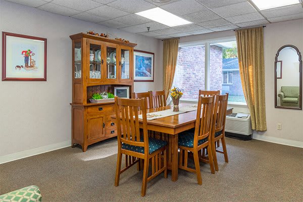 A cozy dining room featuring a wooden table with chairs and a matching cabinet, illuminated by natural light from a large window.