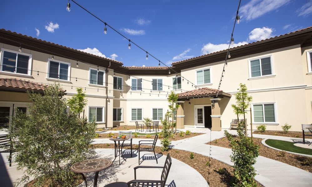 A sunny courtyard with outdoor seating and string lights at a modern residential building.