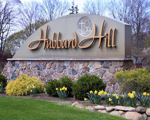 Entrance sign for Hubbard Hill surrounded by blooming daffodils and greenery.