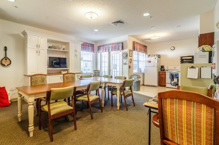 A spacious dining and kitchen area with multiple tables and chairs, well-lit with natural light from large windows.