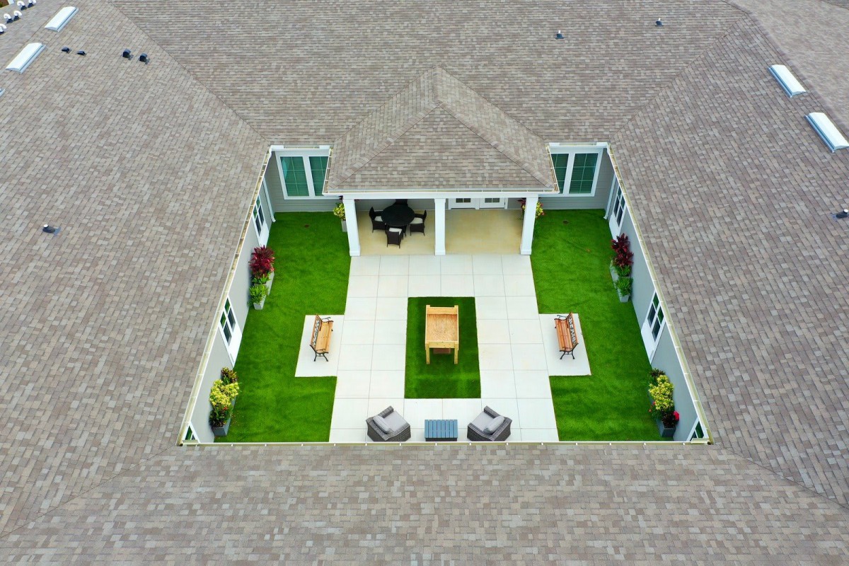 An aerial view of a courtyard design within a house, featuring green spaces and outdoor furniture.