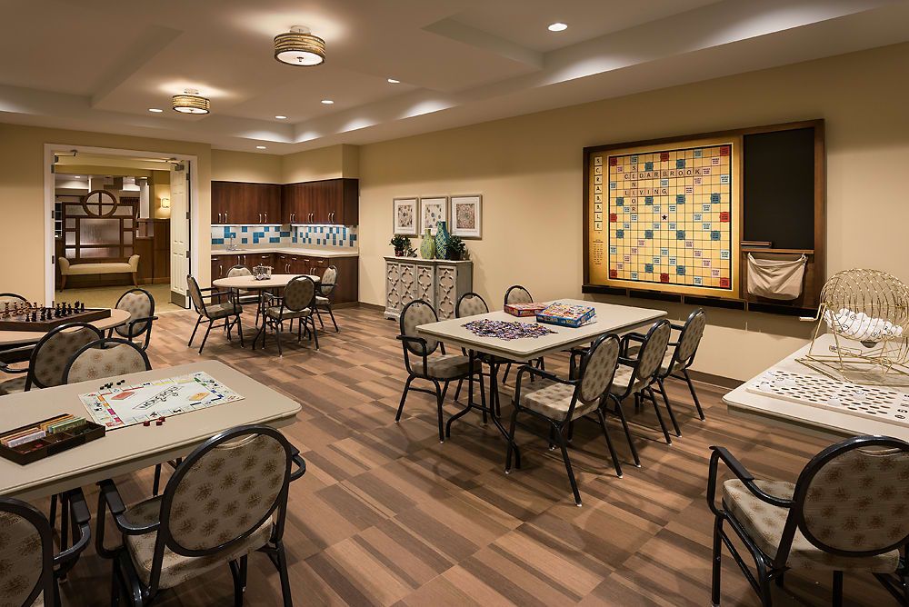 A community game room featuring tables and chairs, with a large Scrabble board on the wall.