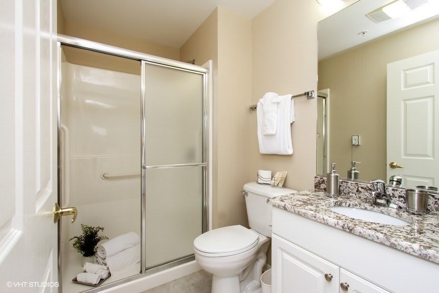 A modern bathroom featuring a glass shower, toilet, and sink with a mirror and neatly arranged towels.