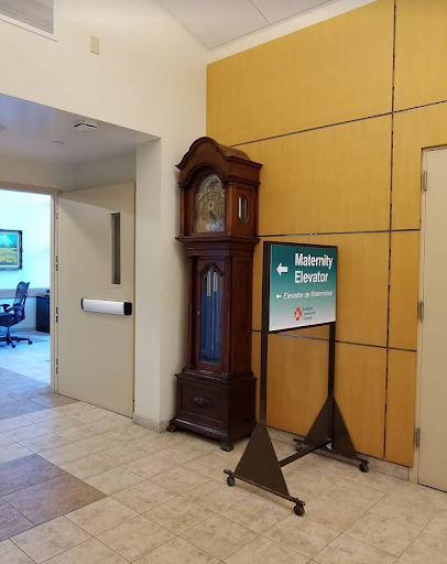 A traditional wooden clock stands beside a directional sign in a modern office interior.