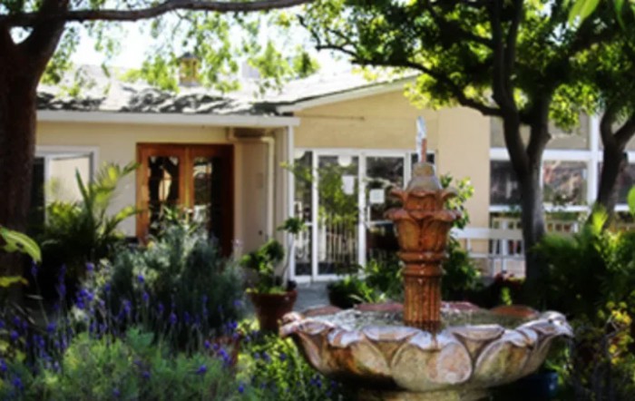 A scenic view of a house entrance with a decorative fountain and lush garden surroundings.