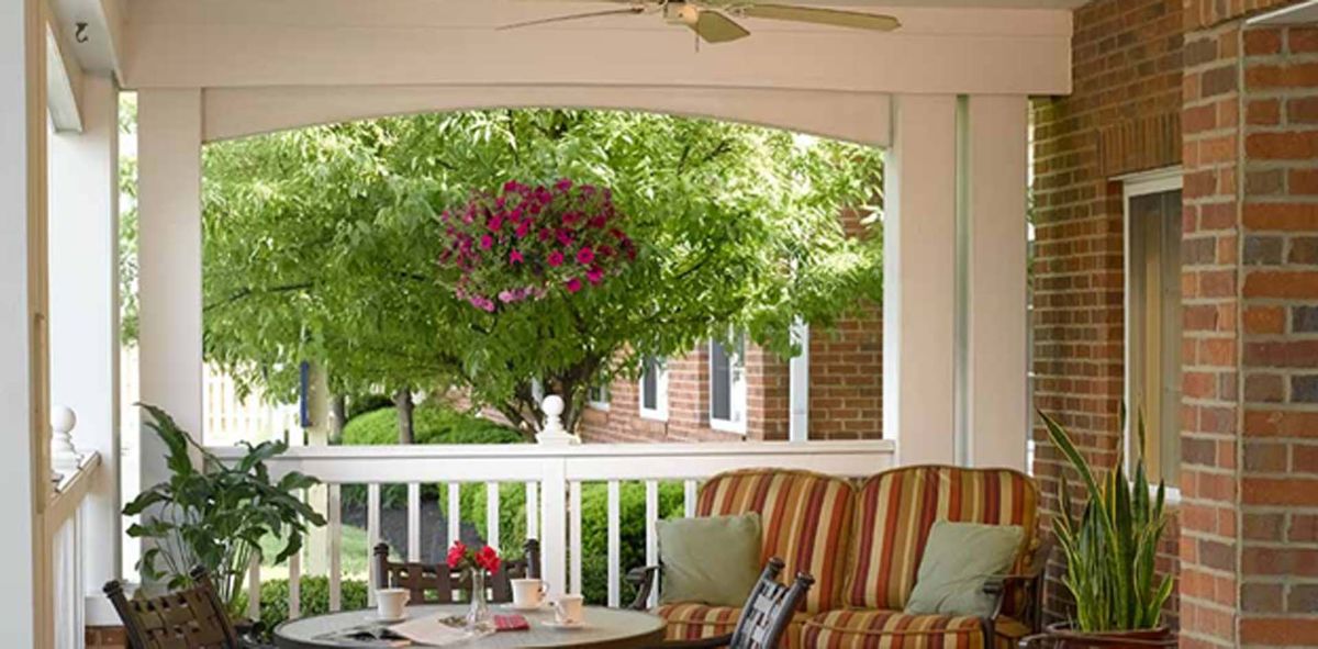 A cozy porch with a striped sofa, a table, and lush greenery in the background.
