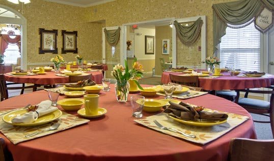 A warmly decorated dining room with tables set for a meal, featuring yellow dinnerware and floral centerpieces.