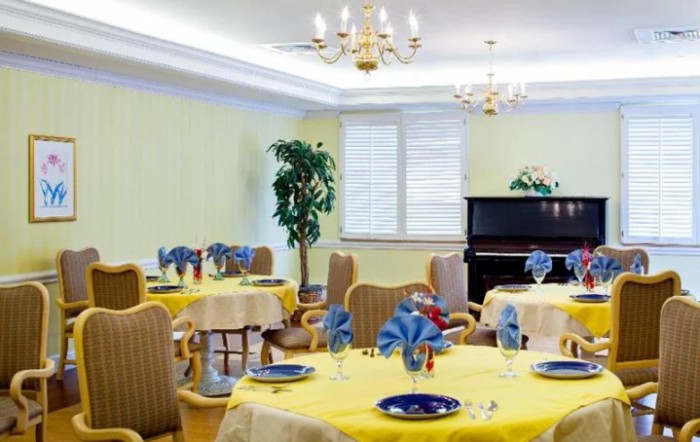 An elegantly decorated dining room with neatly set tables, chandeliers, and a piano in the corner.