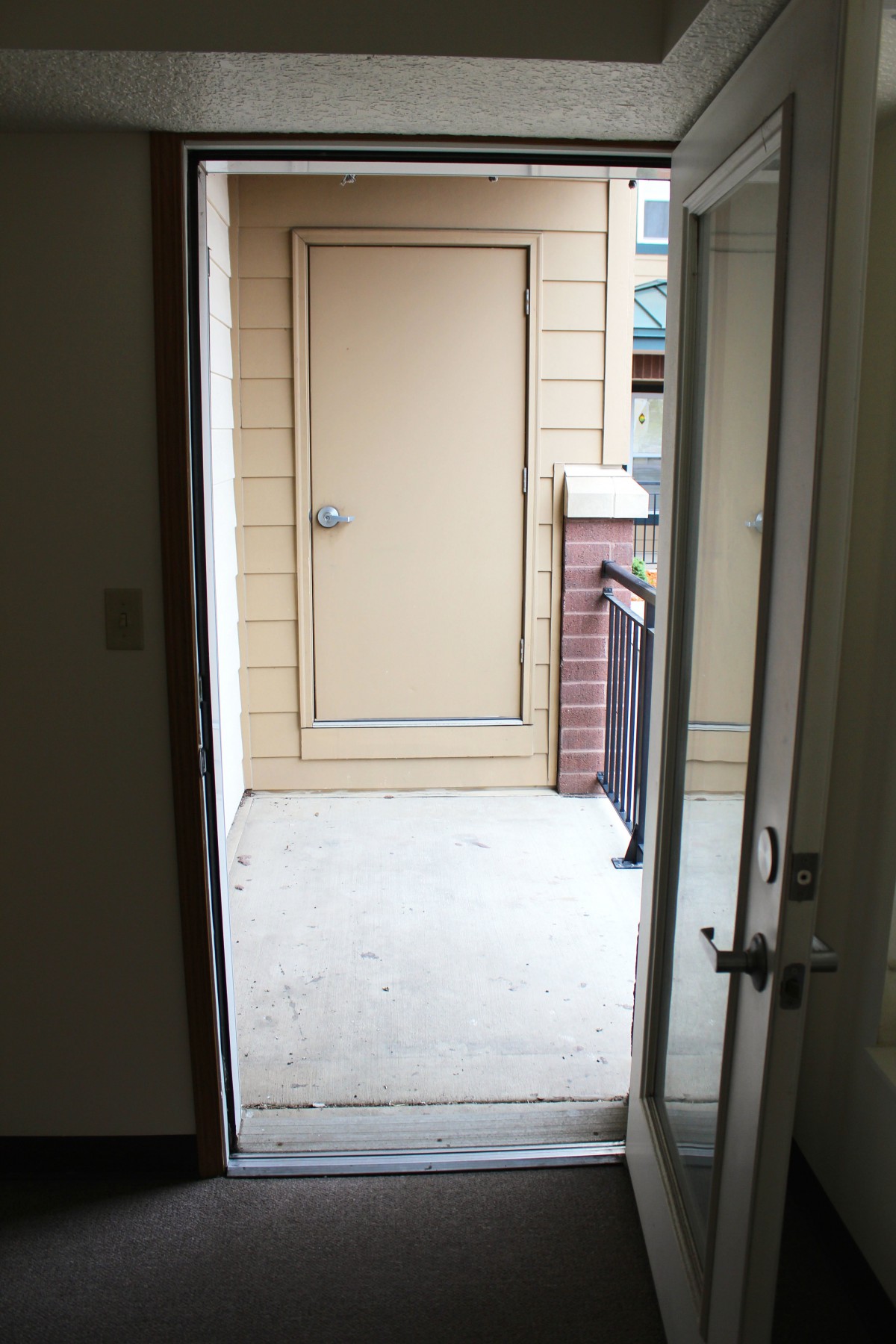 An open door leading to a small patio area with a closed storage door.