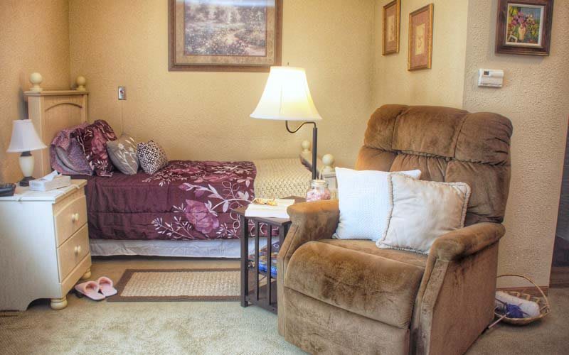 A cozy living room with a comfortable armchair, lamp, and bed.