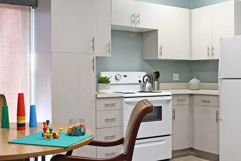 A modern kitchen with white cabinets and a stove, featuring a chair and toys on a table.