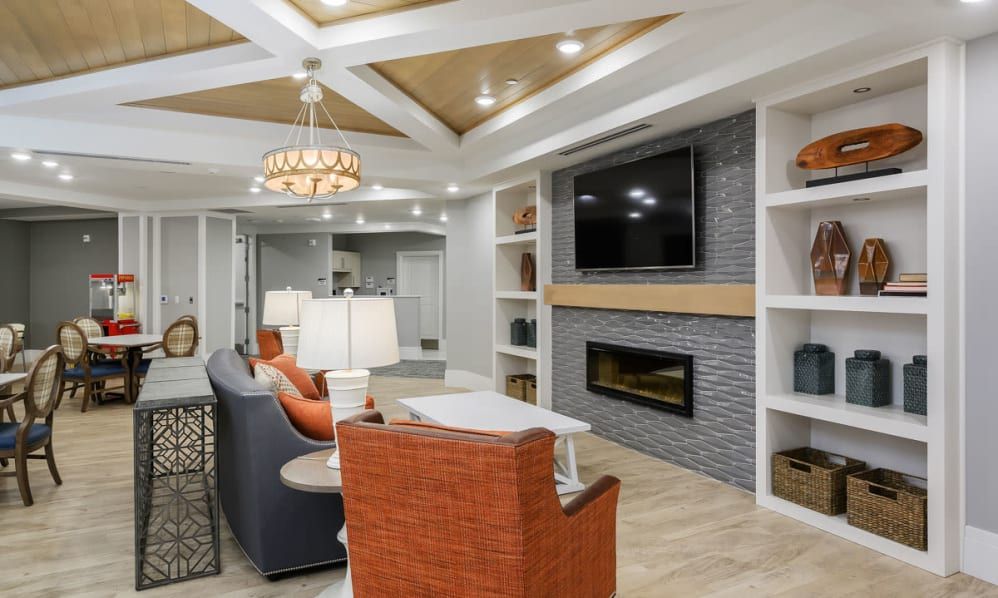 A modern living room featuring a sophisticated ceiling design with recessed lighting, a wall-mounted TV above a sleek fireplace, and comfortable seating arrangements.