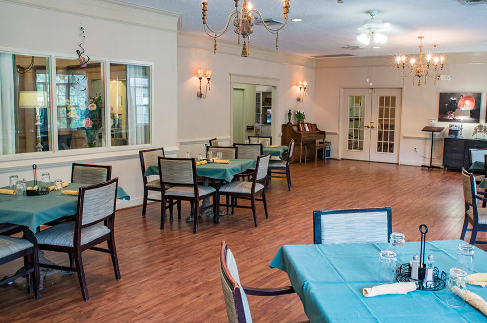 An elegant dining room with neatly arranged tables and chairs, featuring chandeliers and a wooden floor.