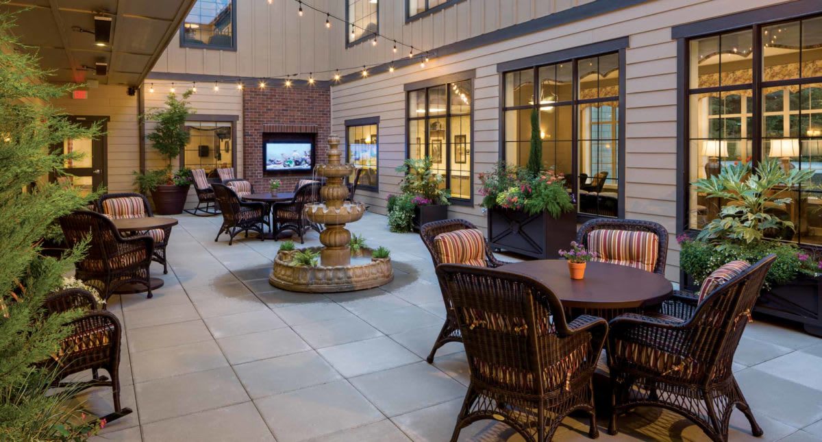 A cozy outdoor courtyard with a fountain and patio furniture, illuminated by string lights.