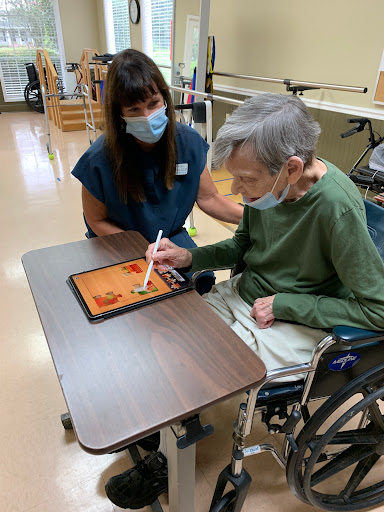 A caregiver assists an elderly person with a tablet, promoting engagement and interaction.