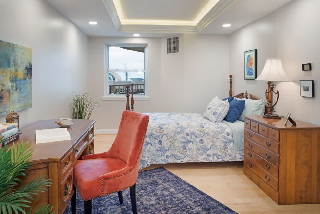A cozy bedroom with a desk, chair, and patterned bedding.