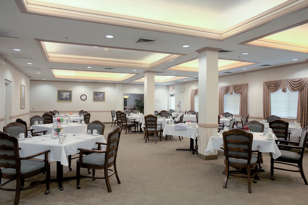 An elegant dining room with neatly set tables and chairs, featuring warm lighting.
