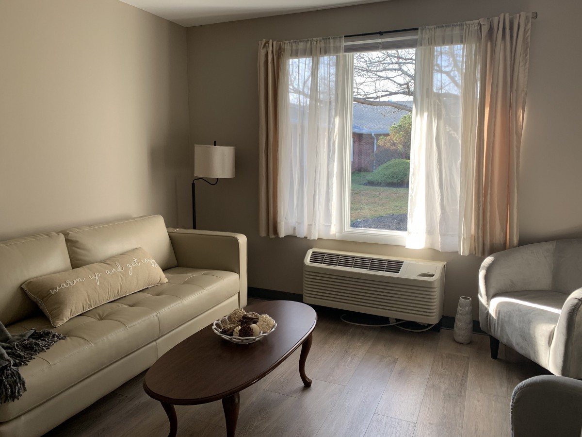 A cozy living room with a sofa, armchair, and coffee table near a large window letting in natural light.
