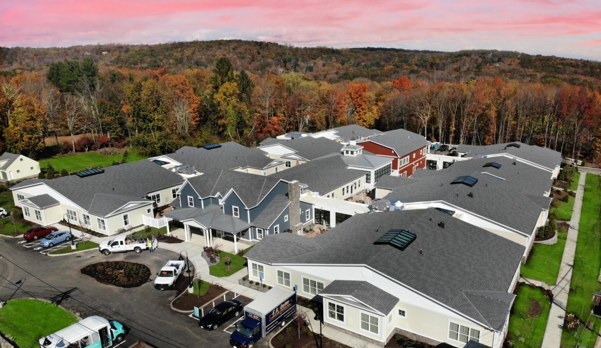 Aerial view of a suburban neighborhood surrounded by autumn foliage under a pink sunset sky.