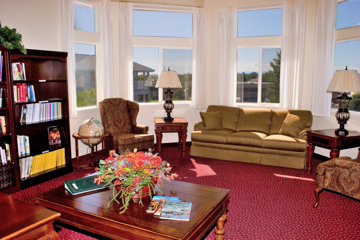 A cozy living room with large windows, featuring a sofa, armchair, and a coffee table decorated with flowers.