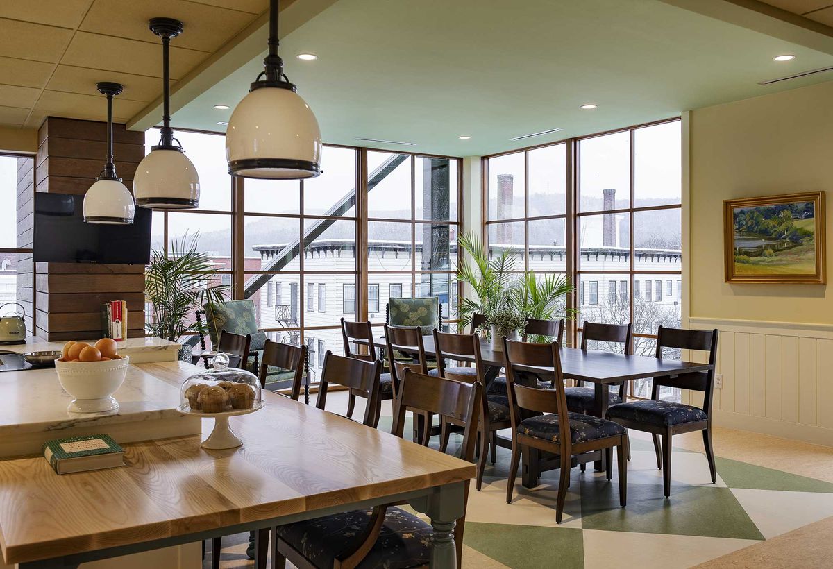 A modern dining space with large windows, wooden tables, and chairs, complemented by indoor plants.