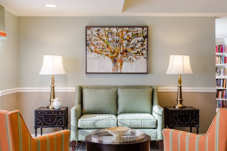 A cozy living room with a green sofa, framed artwork of a tree, and elegant lamps on side tables.