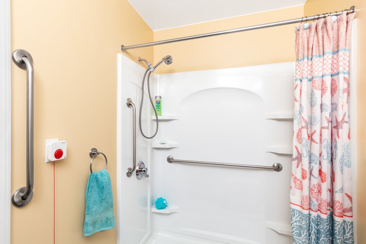 A bathroom featuring a bathtub with a handheld showerhead, grab bar, and colorful curtain.