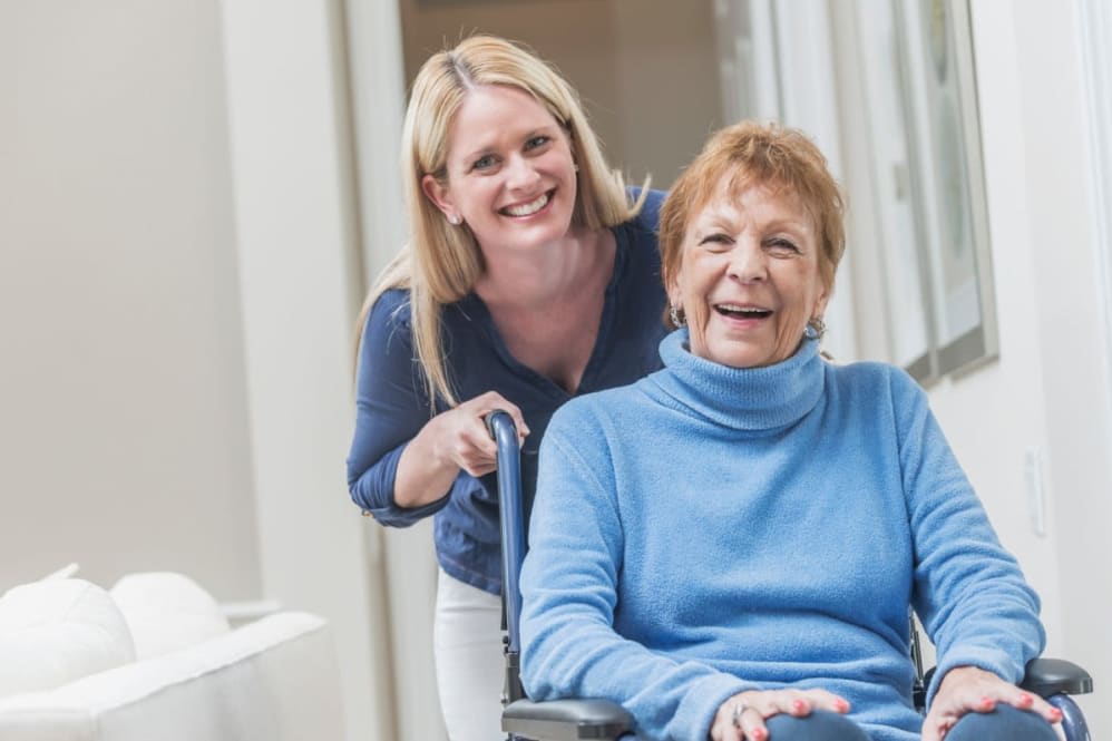 A caregiver smiling with an elderly woman in a wheelchair.