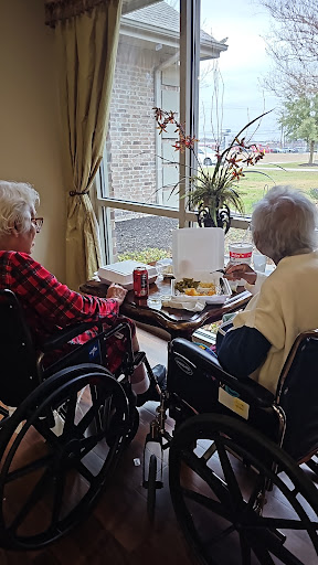 Two elderly women enjoying a snack while seated by the window.