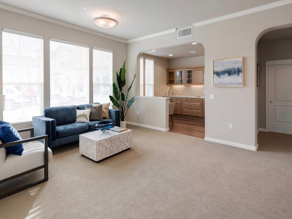 A modern living room with a blue sofa, coffee table, and large windows, leading into a kitchen.