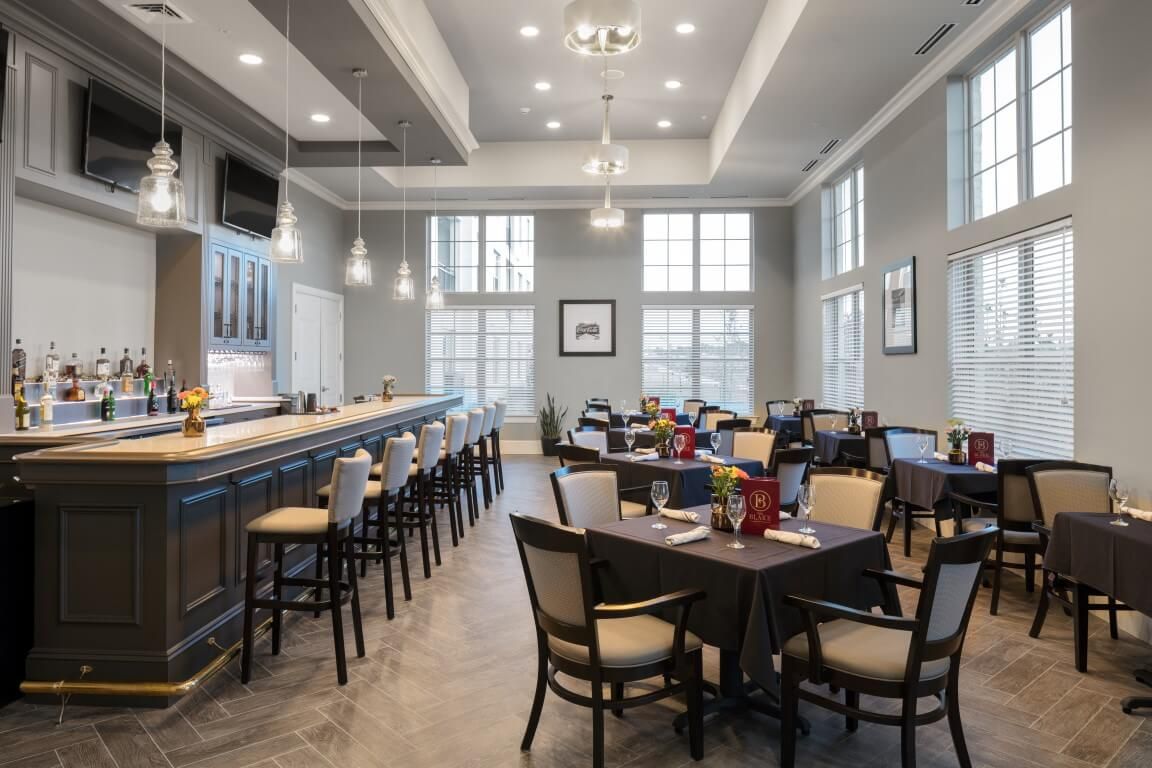 A modern restaurant interior featuring a bar area with high stools and a dining space with several tables and chairs.