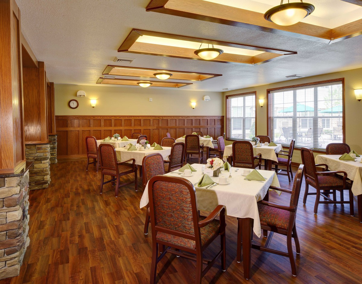 An elegantly set dining room with neatly arranged tables and chairs, featuring a warm wooden floor and soft lighting.