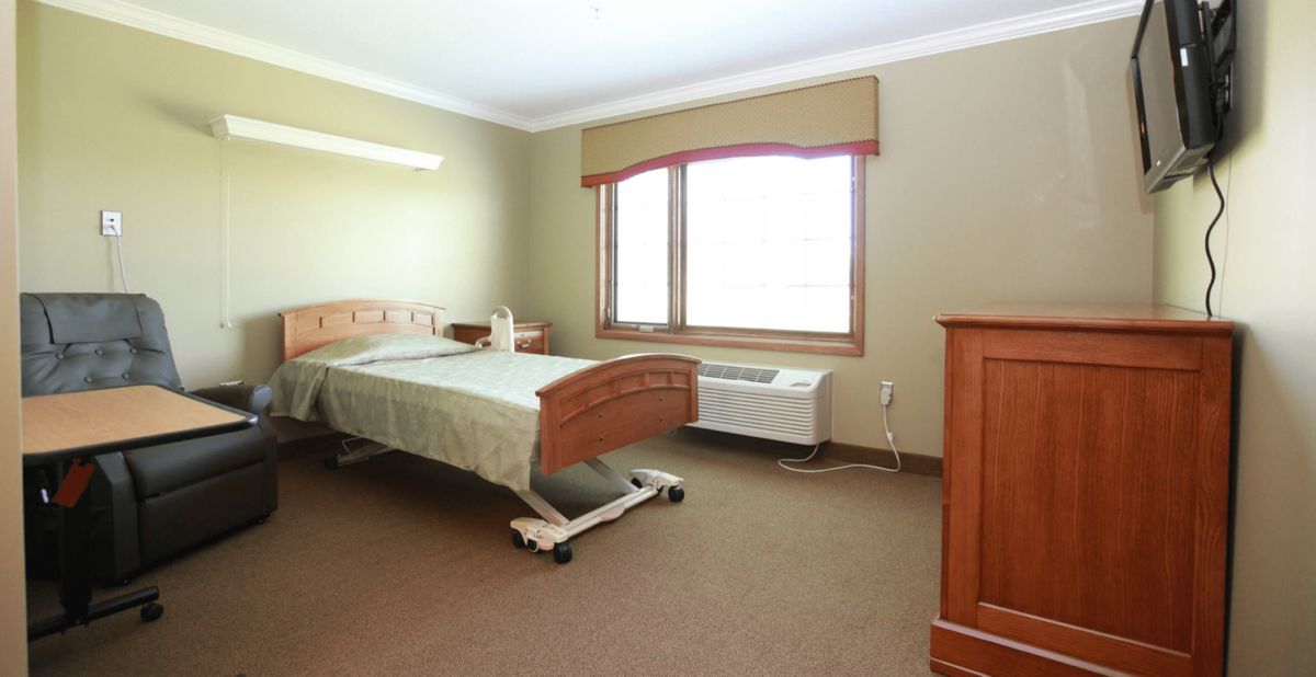 A hospital room with a bed and window, featuring simple furniture.